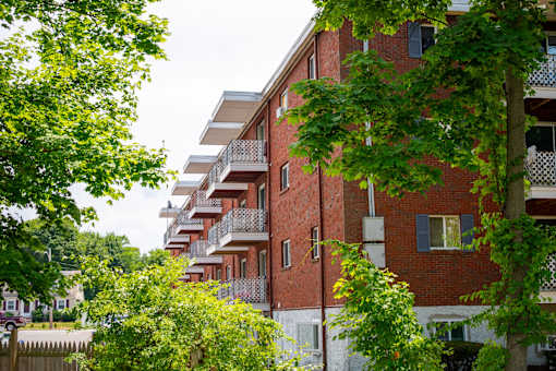 A red brick building with balconies and trees in front.