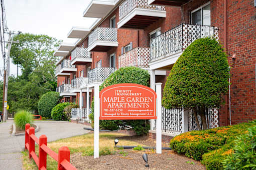 A sign for Maple Garden Apartments is in front of a brick building.