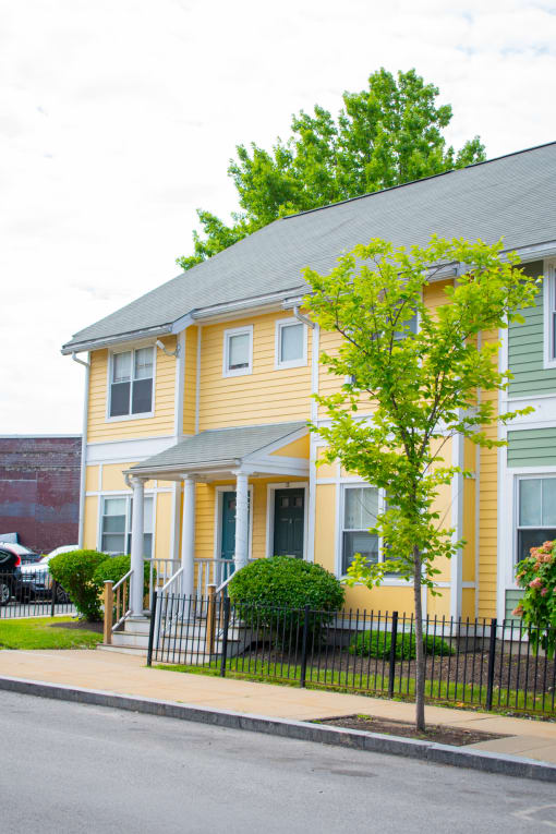 a yellow house with a gray roof and a tree with green leaves in front of it