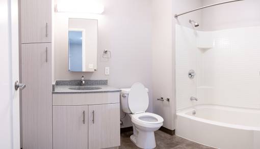A white toilet sits in a bathroom next to a sink and a bathtub.