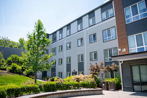 A modern apartment building with a well-maintained lawn and trees in front.