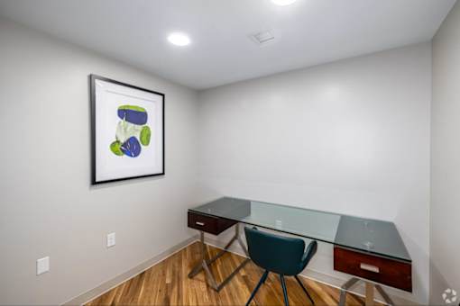 A room with a desk and chair and a picture on the wall.