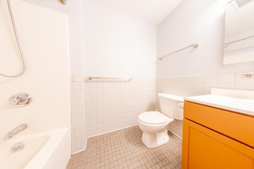 A white toilet sits in a bathroom with a white bathtub and orange cabinet.
