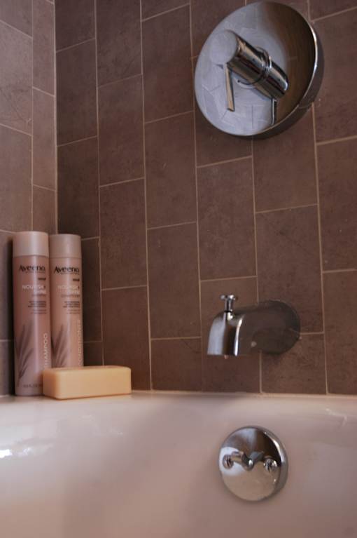 A bathroom with a brown tiled wall and a white bathtub.