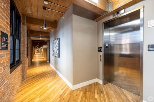 A long hallway with wood floors and a metal elevator.