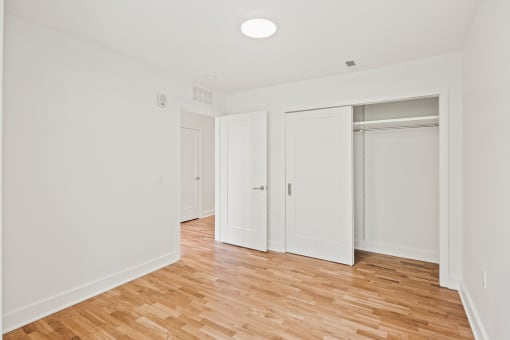 a bedroom with white walls and wood flooring and sliding closet doors