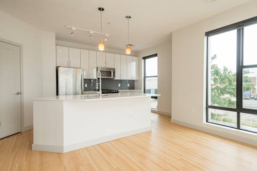 an empty living room with a kitchen in the background