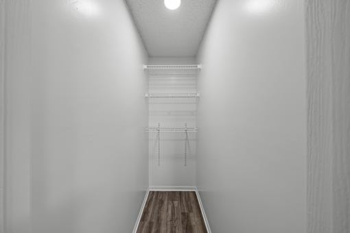 A white room with a wooden floor and a white closet with a shelf and hangers.