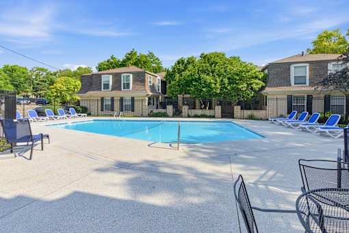 A swimming pool surrounded by lounge chairs and a fence with houses in the background.