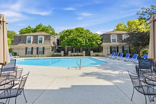 A pool surrounded by chairs and umbrellas with houses in the background.