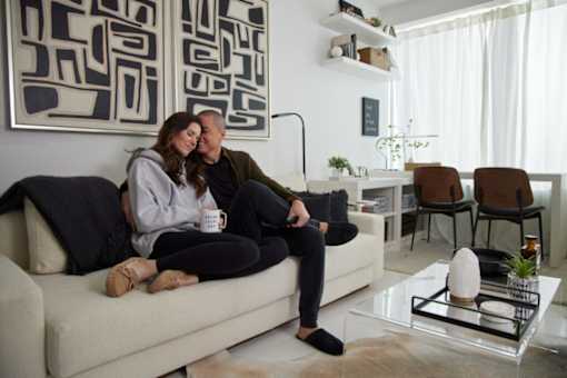 A couple is sitting on a couch in a living room with a large abstract painting on the wall behind them.
