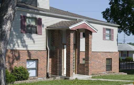 A house with a white siding and a brick facade with a brown door.