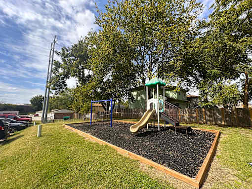 A playground with a green slide and a brown swing set.