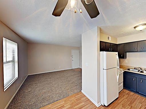 an empty living room with a kitchen with a refrigerator