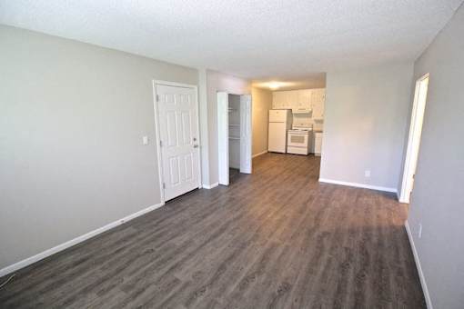 A room with a kitchenette in the back and a door on the left.
