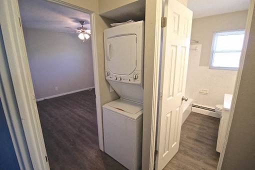 A white toilet is in a small room with a door open to a bathroom.