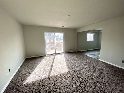 A large empty room with a carpeted floor and a view of a balcony through the door.