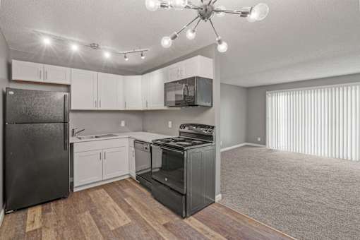 A kitchen with a black refrigerator, white cabinets, and a black stove top oven.