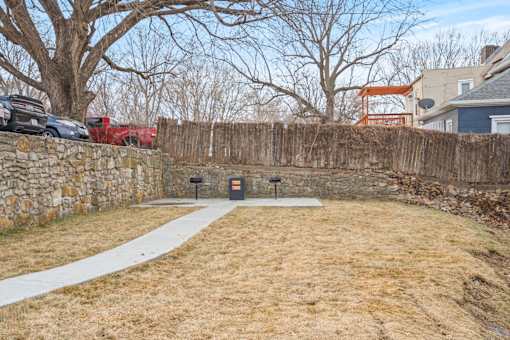 A backyard with a stone wall and a white pathway.