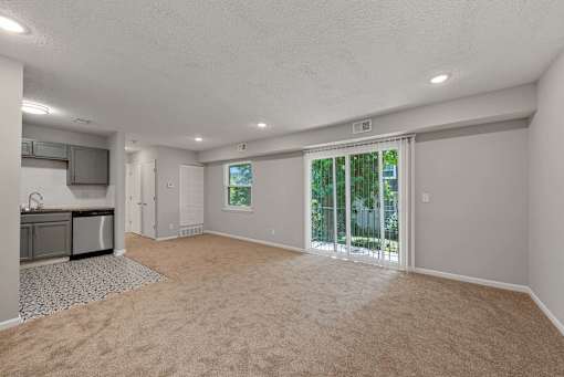 A spacious room with a carpeted floor and sliding glass doors leading to a backyard.