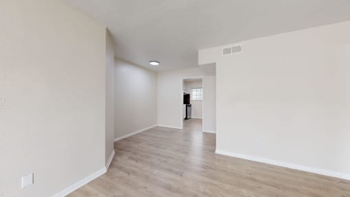 the spacious living room and dining room with white walls and wood flooring
