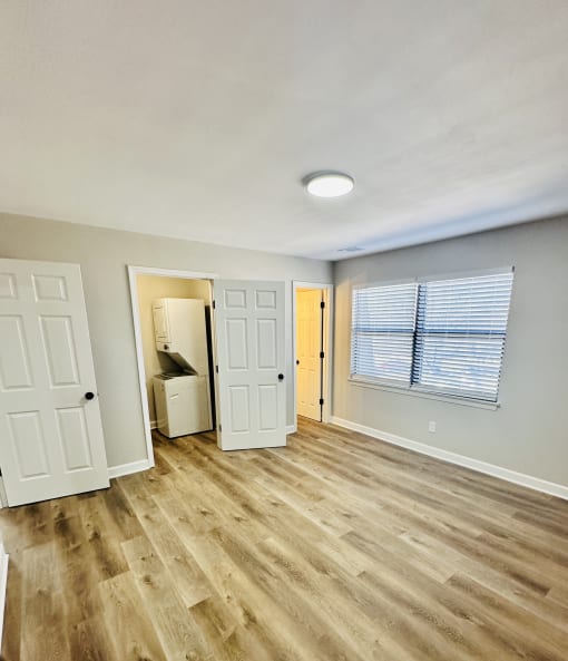 an empty living room with wood flooring and a door to a bathroom