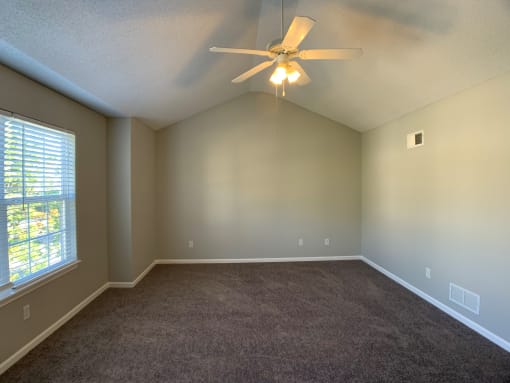 Large carpeted bedroom with ceiling fan and window