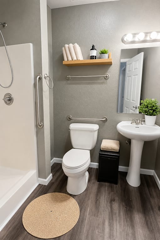 A bathroom with a white toilet, a white sink, and a wooden shelf above the toilet.