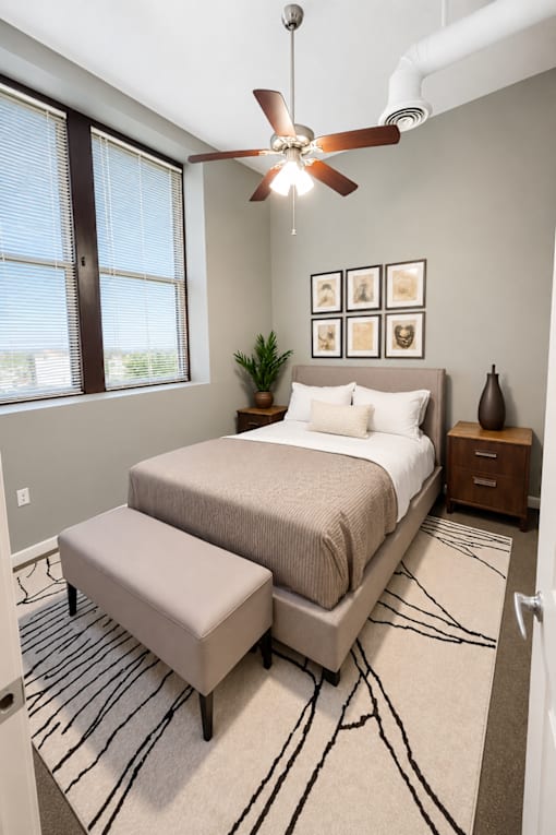 A bedroom with a bed, bench, and a ceiling fan.