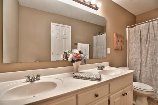 an image of a bathroom with two sinks and a vase of flowers