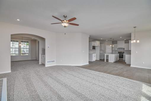 A spacious living room with a ceiling fan and carpeted floor.