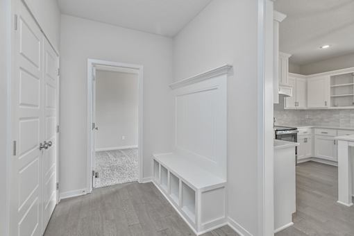 A white room with a bench and a door leading to another room.