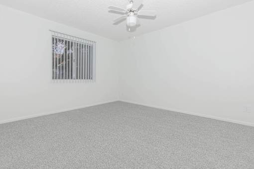 A room with a ceiling fan and a window with bars.