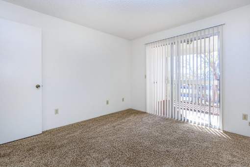 A room with a carpeted floor and a window with blinds.