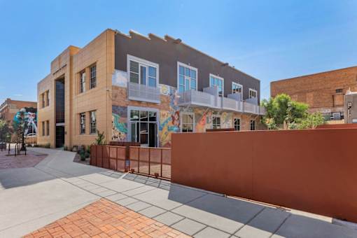 A building with a mural on the side has a red fence in front of it.