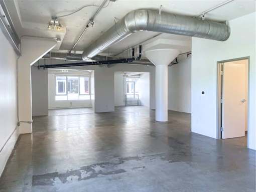 A large empty room with a concrete floor and a long pipe running along the ceiling.