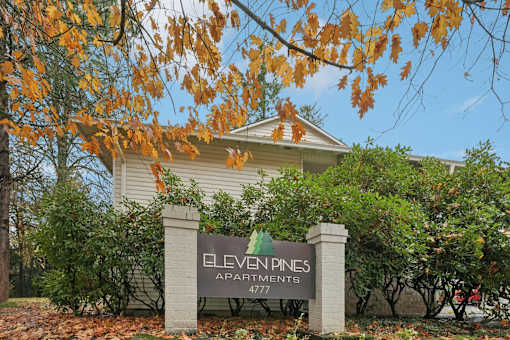 A sign for Eleven Pines Apartments stands in front of a building.