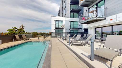 A swimming pool is surrounded by lounge chairs on a patio.