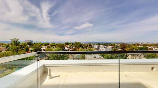 A balcony with a glass railing overlooks a cityscape.