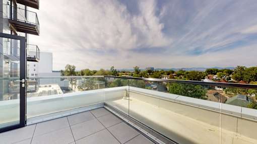 A balcony with glass railings overlooks a residential area.