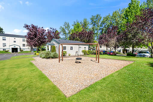 A playground area with a swing set and a sandbox in the middle of a grassy area.