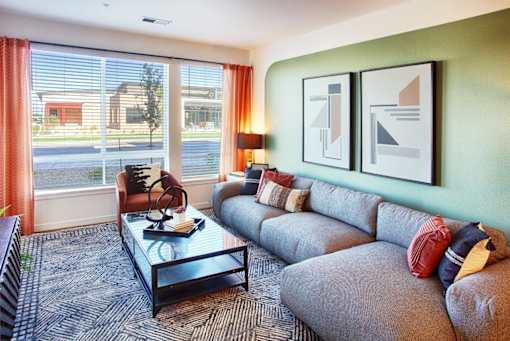 A living room with a grey couch, a glass coffee table, and two framed artworks on the wall.