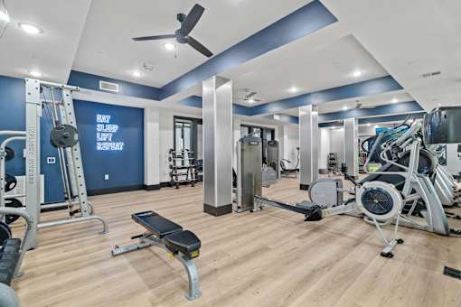 A gym with a variety of equipment including a weight bench, a treadmill, and a fan.