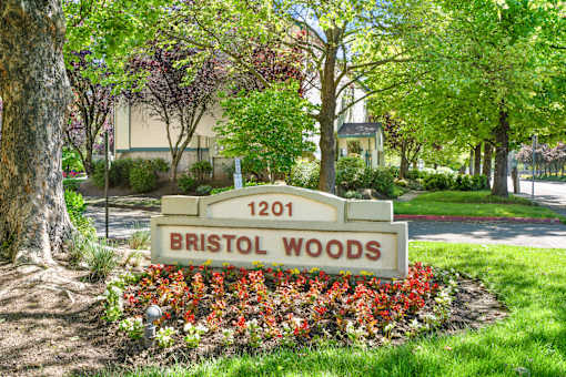 A sign for Bristol Woods is in front of a tree and flowers.