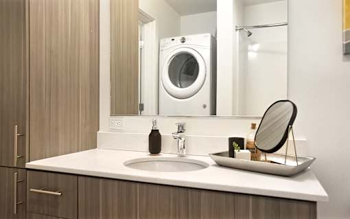 A modern bathroom with a sink, mirror, and a washing machine.