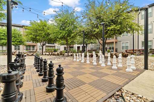 A giant chess board with black and white pieces in the middle of a park.