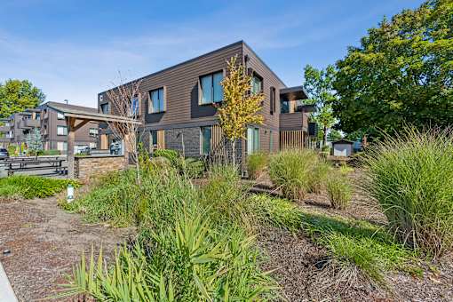 A modern house with a brown exterior and a well-maintained garden in front.