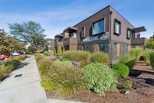 A modern building with the sign "NowLeasing Edition" is surrounded by a variety of plants and trees.