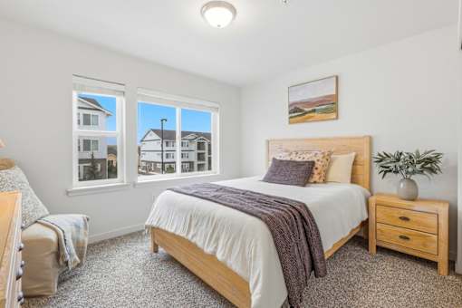 A bedroom with a large bed, a window with a view of a house, and a potted plant on the nightstand.