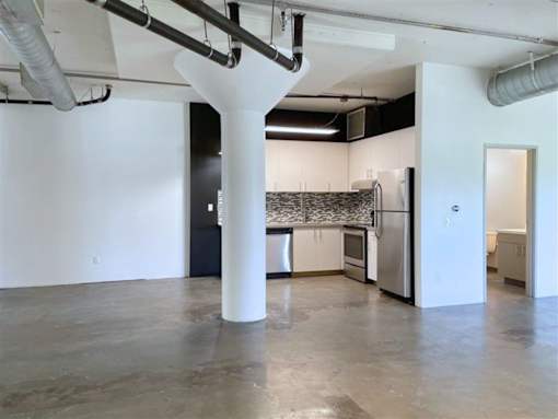 A large white column in the middle of a room with a kitchen in the background.